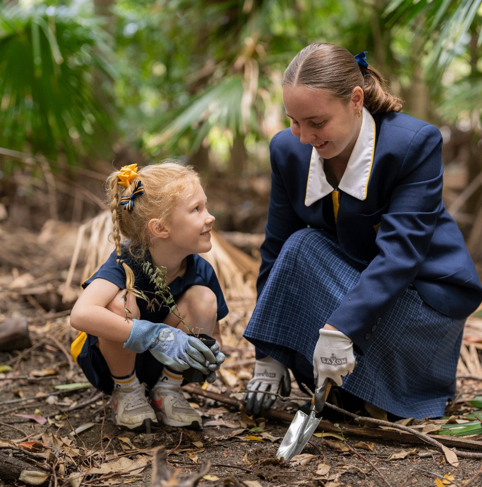 Immanuel senior student mentoring a younger student planting in the rainforest
